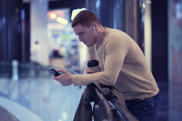 young man using smartphone and listens to music in bluetooth headphones. lonely man in autumn...
