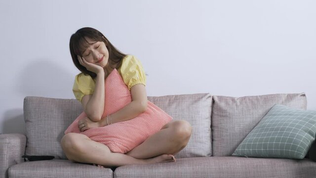 front portrait female holding a pillow is touching her tilting head with an envious look while watching a moving love story film on the couch.