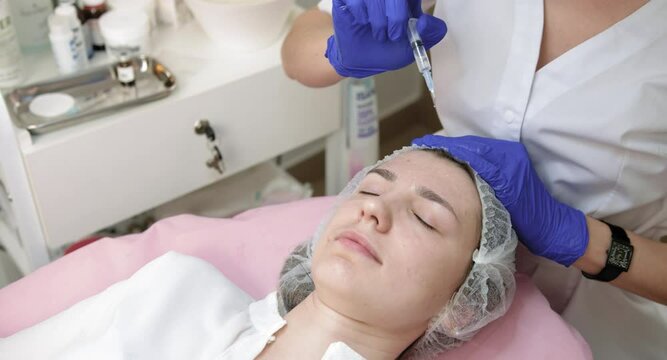 Anti aging and anti wrinkle therapy. Skin care and beauty. Close up of female doctor beautician, applying cosmetic serum on woman's face at modern cosmetology center.