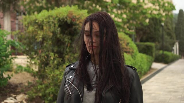 Depressed caucasian woman with long shaggy black hair in the leather jacket apathetic looking at camera