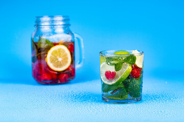 Cocktail in glass with lemon, lime, mint and raspberries on aqua blue background.