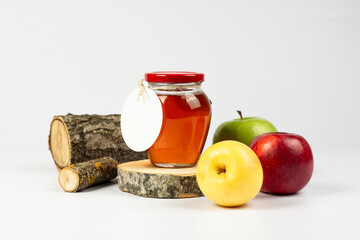 Homemade natural jam. Transparent glass jar with jam inside on cross cut wooden logs and apples isolated on white background. Part of set.