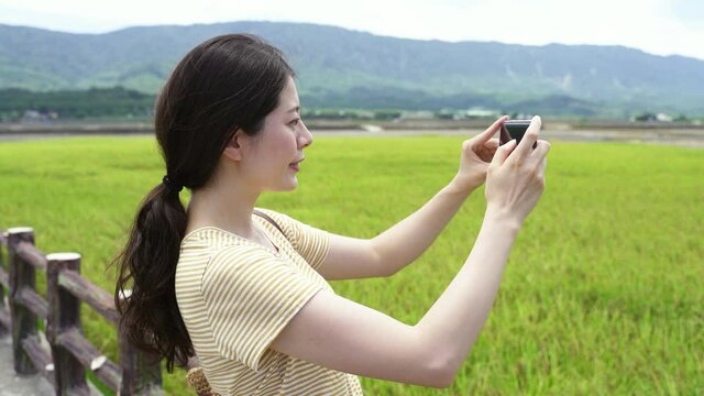 portrait asian woman tourist is capturing the image of beautiful landscape with her smartphone near a green meadow on a clear day in the summer at dapo pond.