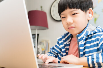 Online learning programs concept. Portrait of a cute and smart asian student boy with wireless earbuds using tablet computer to join online classroom from home during Covid-19 pandemic. New normal.