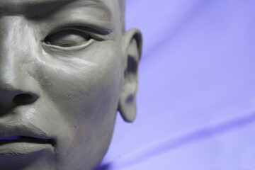 Face detail. Clay Sculpture in process of creation, Asian features, on lilac background