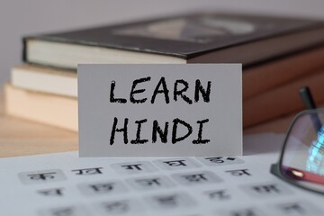 A card with the text LEARN HINDI written on a card on office desk with HINDI alphabet letters page....