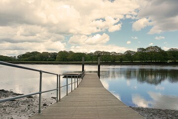Fototapeta premium jetty boardwalk over quiet river. Cloudy day in the UK