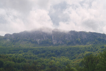 Mountain landscape and clouds passing over the peek, and green summer forest in the bottom
