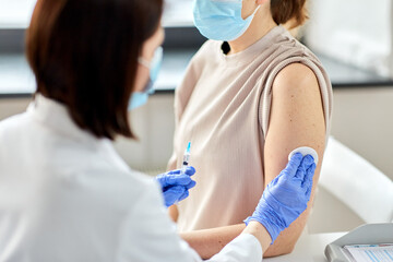 Fototapeta premium health, medicine and pandemic concept - close up of female doctor or nurse wearing protective medical gloves with syringe vaccinating patient at hospital