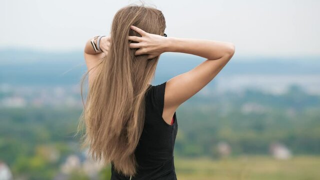 Closeup of long free falling female hair waving on light wind on her shoulders outdoors.