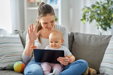 family, motherhood and people concept - happy smiling mother with little baby daughter having video call on tablet pc computer at home