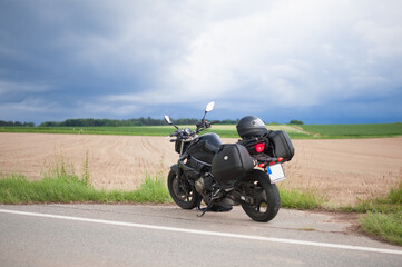 naked unrecognizable black motorcycle with suitcases on the sides stands on the side of the harvested field