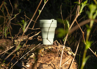 Reusable silicon coffee cup in forest among green plants, trees. Eco lifestyle.
