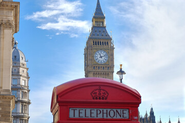 typical red phone box on the streets of london with big ben looming behind, united kingdom