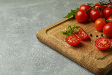 Cutting board with cherry tomato on gray textured background