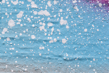 Macro close-up of a spray painted turquoise and light gray wall with white and purple spray paint splashes. Abstract full frame textured splattered graffiti background with copy space.