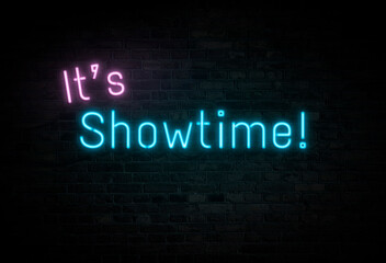 Illuminated and glowing pink and blue "It's Showtime!" neon sign on dark brick wall.