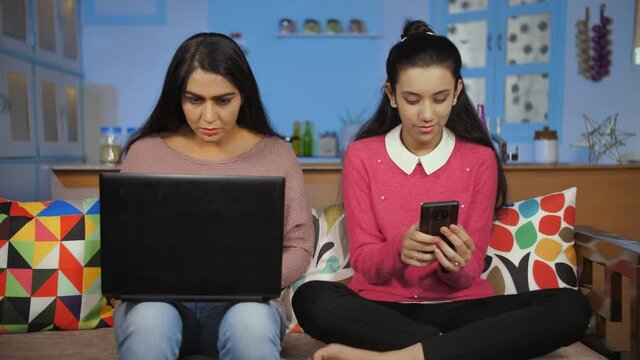 Mother And Daughter Busy Using Laptop And Mobile At Home - Disconnected Family. Use Of Modern Technology In Our Lives - Screen Time. Female Working From Home And Teenager Busy On The Phone