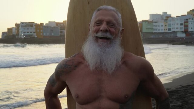 Senior man having fun surfing at sunset time - Sporty fit male training with surfboard on the beach - Elderly healthy people lifestyle and extreme sport concept