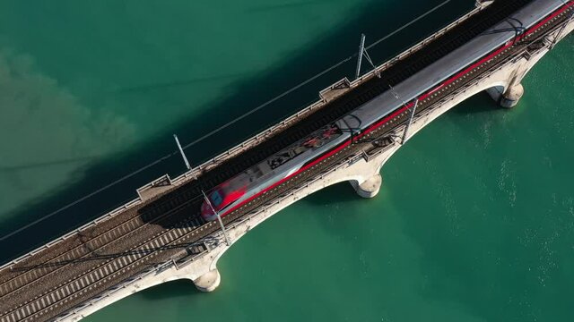 Red high-speed train top view, slow motion on an arched bridge over a mountain river in Italy. Arched bridge over the water. Train on the bridge over the river aerial view. Red train in Europe.