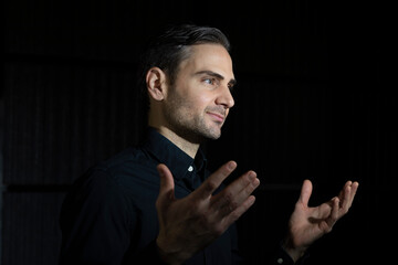 An influencer, artist and musician, dress with black shirt, poses for the camera in one of his photographic shootings for social networks, in a dark backstage area, at night, in Spain.