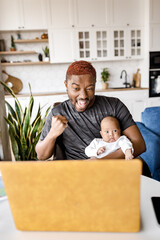 Overjoyed Afro American working dad with baby son looking at laptop screen, celebrating online successful and unbelievable news at office. Emotional millennial guy getting dream job offer