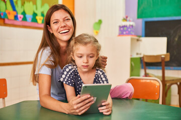 Happy childminder and girl at the tablet computer