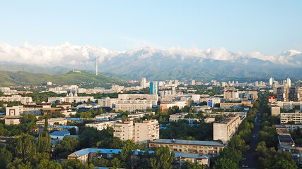 Fototapeta na wymiar Bright color sunset over the city of Almaty. Huge clouds over the mountains and the city shimmer from bright blue to yellow and dark blue. Tall houses and green trees, cars driving on the roads.