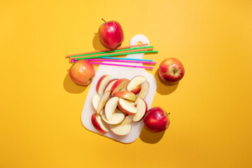 Chopped red apple on a board. Orange background and straws. Minimal concept.