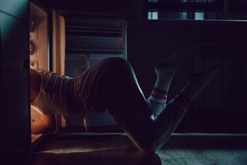 Fototapeta na wymiar The woman looks into the refrigerator in search of food late at night. Hunger concept