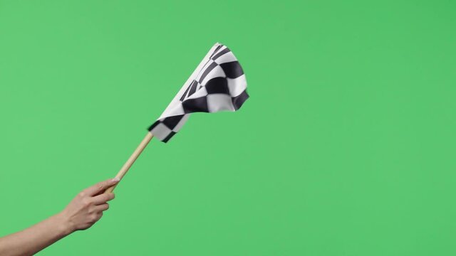 Female hand holding and waving checkered race flag in slow motion against green screen background. Victory, achievement, success, sport concept. Silk black and white checkered flag finish start race.
