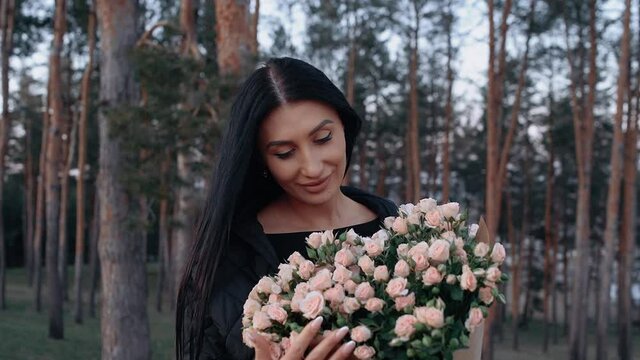 The happy woman smells the bouquet of white roses, in the bosom of nature, on the green meadow, near the table for the romantic dinner