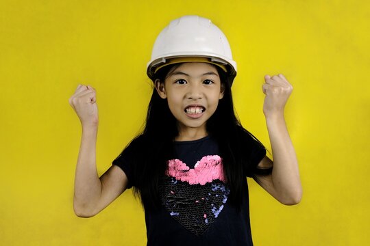 A half body shot of a cute young Asian girl wearing a white hard hat or construction helmet, getting ready to go to inside an construction site.