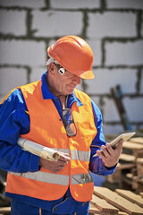 Senior Man holding blueprints and using tablet on construction site