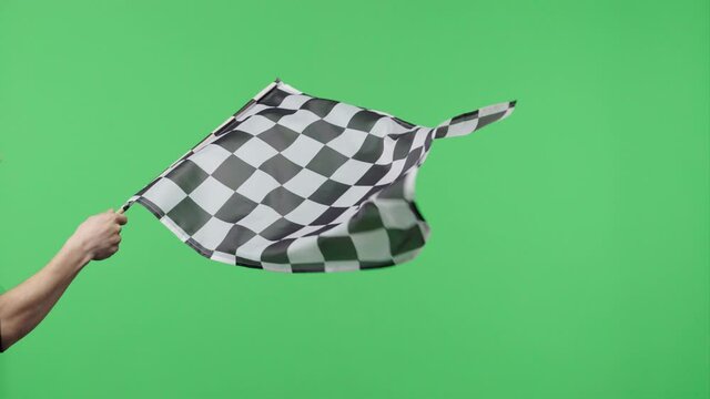 Male hand holding and waving checkered race flag in slow motion against green screen background. Silk black and white checkered flag finish start race. Victory, achievement, success and sport concept.