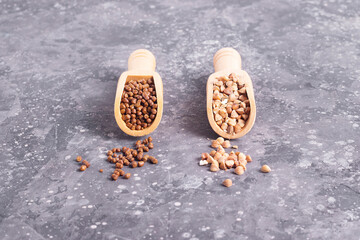 Buckwheat tea granules and raw buckwheat in wooden spoons on gray background