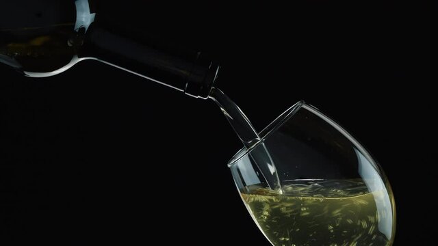 Wine. Pouring white wine from the bottle on black background. Wine splashing in a wineglass.