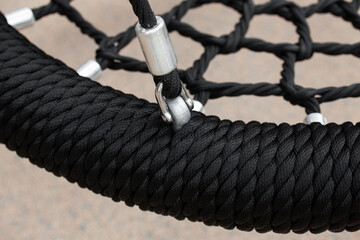 Black rope circle swing seat at the playground close-up. Black net swing bench on a kids playground.   Modern urban environment. © alexburakov12