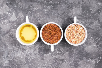 Raw buckwheat, buckwheat tea granules and brewed tea in white cups on a gray background