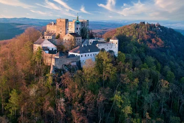  Buchlov Castle. Aerial view on monumental castle in Romanesque Gothic style, standing on a wooded hill against Saint Barbara’s Chapel on the hill in background. Spring, tourism hot spot. Czech castles © Martin Mecnarowski