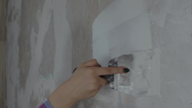 Close up of unrecognizable person applying putty on wall in room. Unknown woman plastering wall with spatula in apartment. Concept of repair work and improvement of housing conditions.
