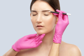 Make-up artist makes markings with white pencil for eyebrow and paints eyebrows. Professional makeup and facial care.