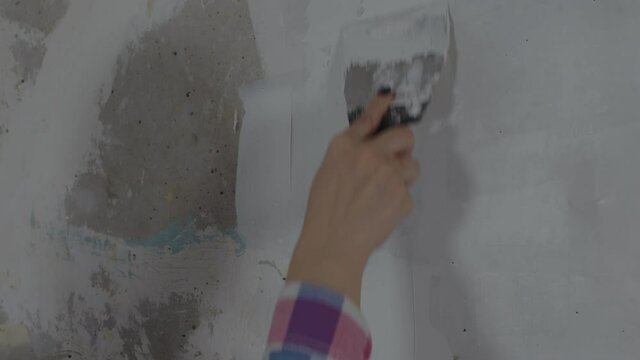 Close up of unrecognizable person applying putty on wall in room. Unknown woman plastering wall with spatula in apartment. Concept of repair work and improvement of housing conditions.