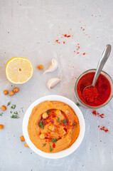 Flat lay of a bowl of delicious hummus with olive oil, garlic and paprika on a grey background.