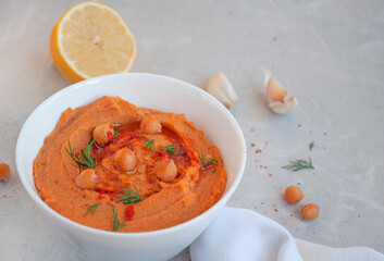 A bowl of delicious hummus with olive oil, garlic and paprika on a grey background.
