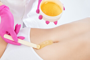 A beautician makes a sugar paste depilation of a woman's belly in a beauty salon. Female aesthetic...
