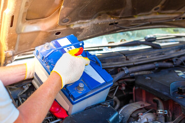 Maintenance of the machine. A male car mechanic takes out a battery from under the hood of a auto...