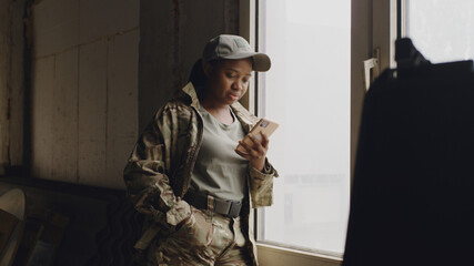 African American female soldier using smartphone near window