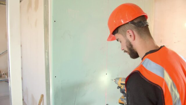 Male contractor in hardhat installing drywall during renovation