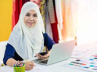 Islamic dressmaker using smartphone and making notes